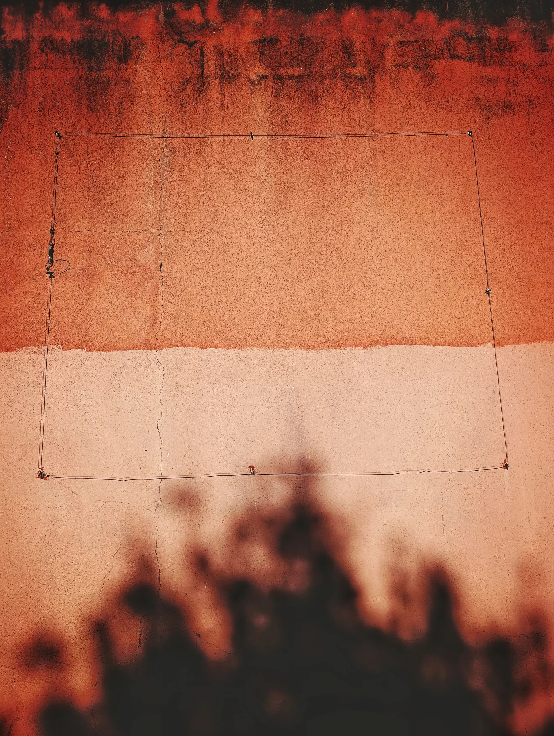 Shadows on a rust-orange and pink wall, framed by a loop of wire